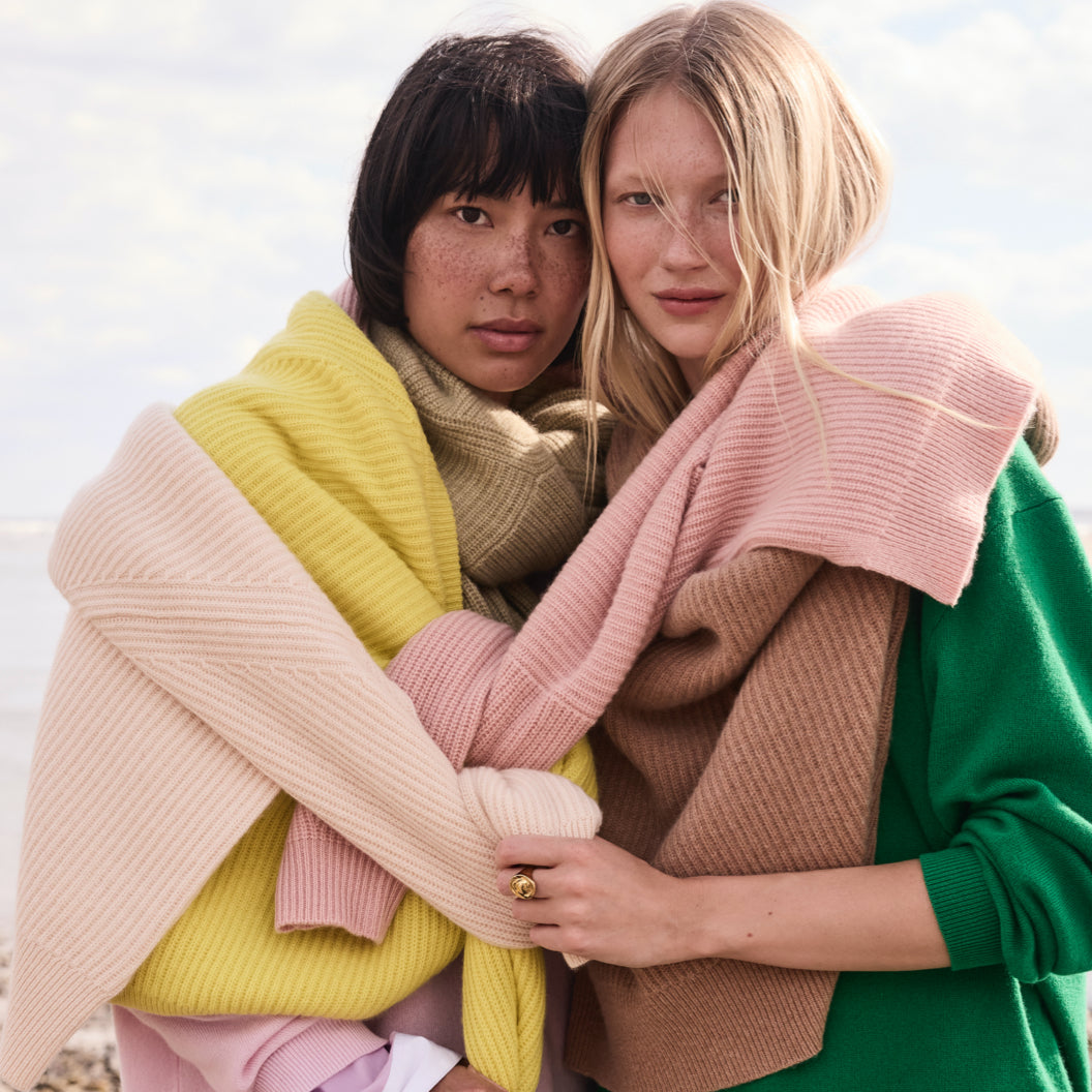Two individuals wrapped in J.Crew cashmere sweaters in pink, yellow, tan, and green