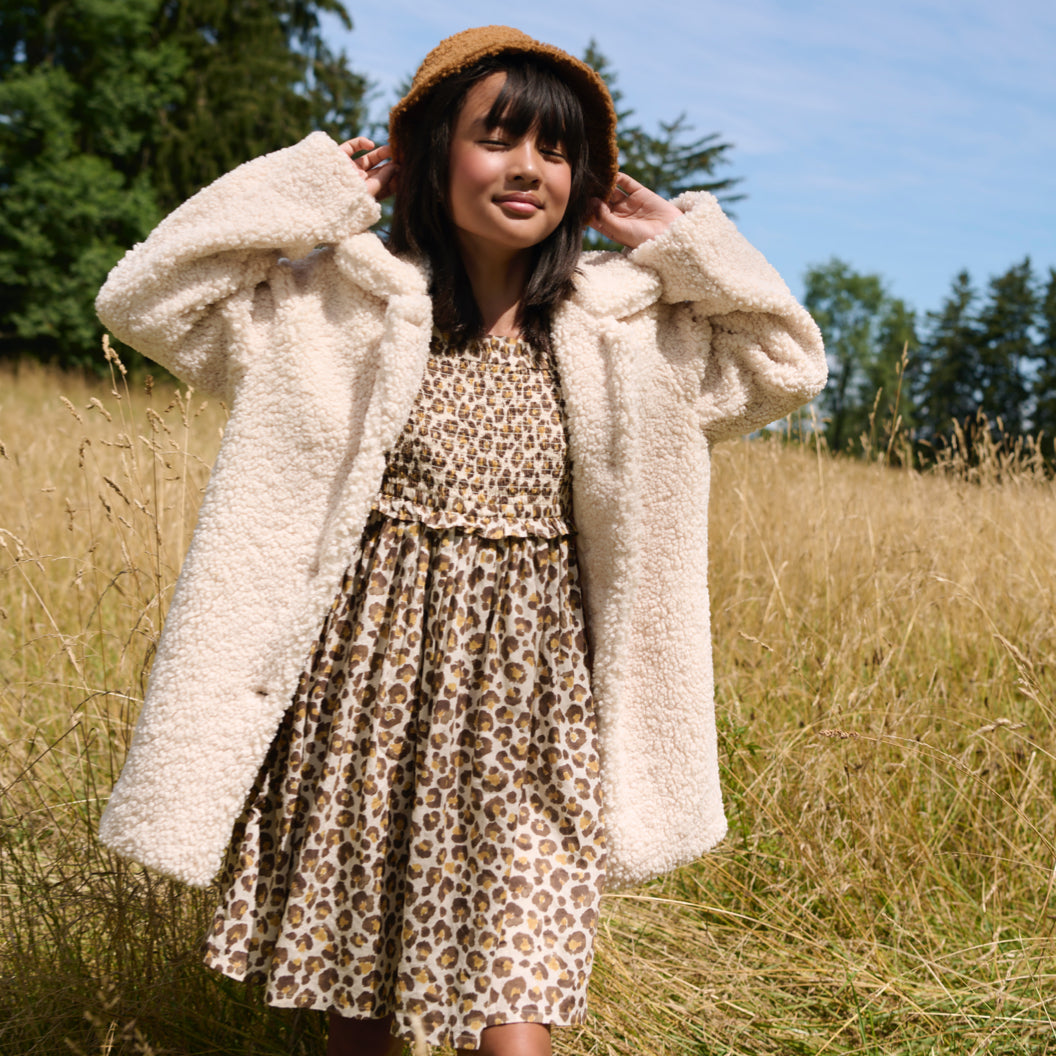 Child wearing a leopard print J.Crew dress, a sherpa coat, and a sherpa bucket hat